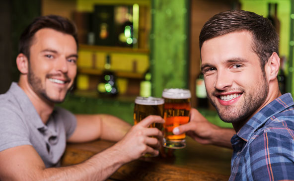 Zwei lächelnde junge Herren stoßen in einem Pub mit 2 Gläsern Bier an