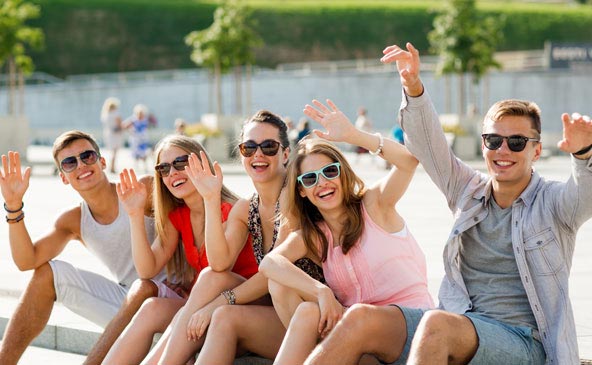 Fünf Freunde mit Sonnenbrille auf einer Freitreppe, beim Lachen und Winken 