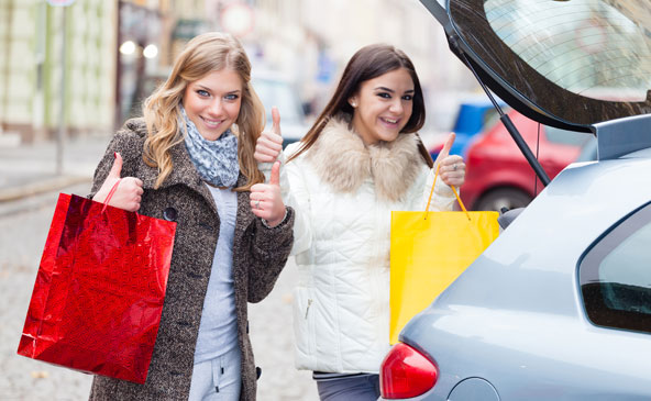 Zwei junge Damen mit Einkaufstaschen beim Laden des Kofferraumes des Auto zeigen alles OK mit erhobenen Daumen