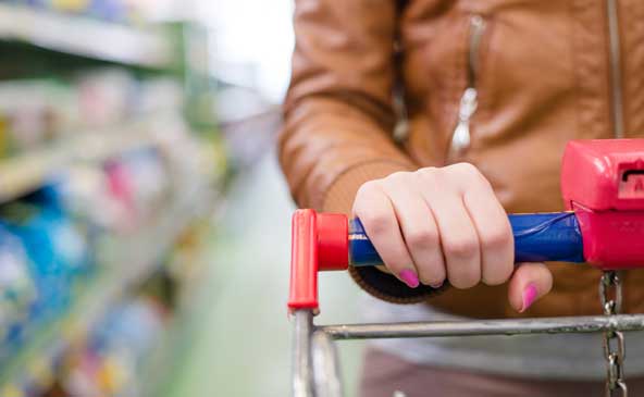 Dettaglio della mano di una donna con unghie tinte di rosa che spinge un carrello al supermercato