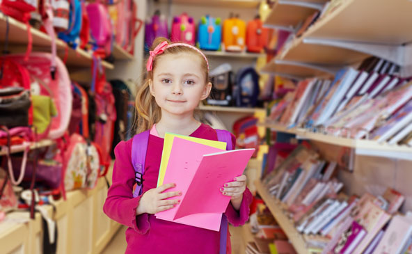 Kleines in rosa gekleidetes Mädchen mit Schultasche hat in einer Schreibwarenhandlung Bastelmaterial in der Hand