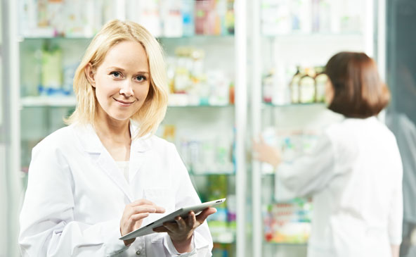 Farmacista con tablet davanti ad armadio di vetro con farmaci