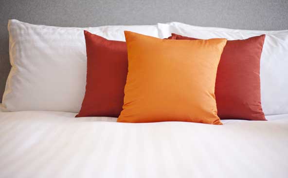 Nahaufnahme eines Bettes mit den 2 weißen Kopfpolstern und roten und orangen kleinen Kissen