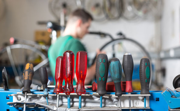 Eine Vielzahl an Schraubenziehern perfekt geordnet mit Handwerker im Hintergrund, der gerade ein Fahrrad repariert