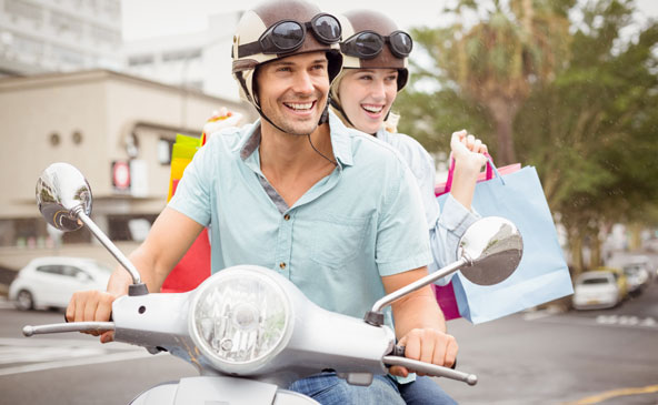 Junges Paar mit Helm und Einkaufstaschen auf einem Vespa-Roller