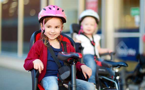 Zwei kleine Mädchen mit Helm auf dem Sicherheitssitz von zwei Fahrrädern