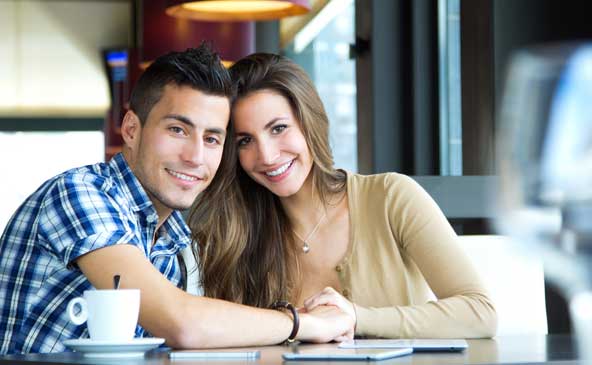 Giovane coppia che sorride e si tiene per mano seduta a un tavolo