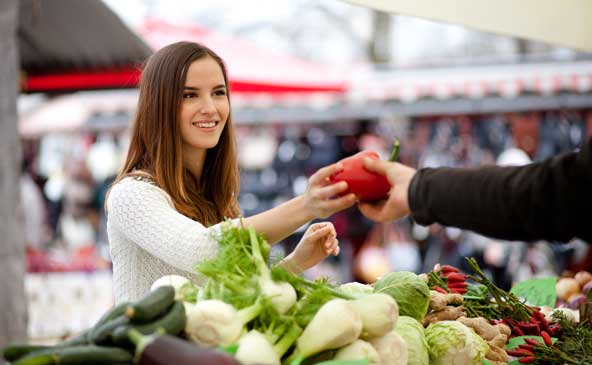 Giovane donna che prende un peperone rosso da un fruttivendolo al mercato